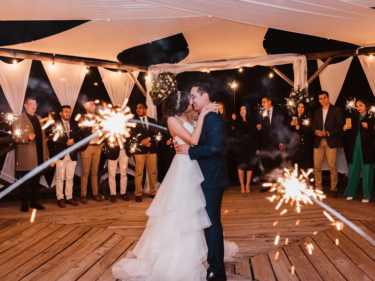 Novios besándose rodeados de invitados con bengalas